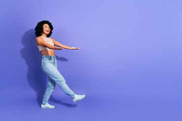 Obraz premium Cheerful young woman with curly hair dancing in a colorful casual outfit against a vibrant purple background