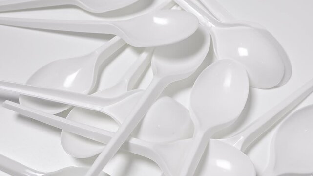 Disposable plastic spoon on rotating white background. Concept of global environmental problems, waste reduction, recycling of non-biodegradable trash, overconsumption, carbon footprint. 