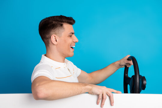 Young man with a steering wheel playfully pretending to drive on a blue background, creating a cheerful and dynamic moment