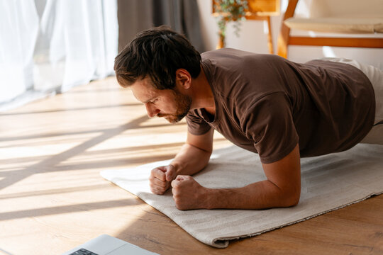 Focused handsome man doing core strength plank exercise indoors at home in modern living room