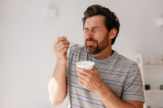 Middle aged, bearded man reacting with disgust while eating unpleasant yogurt - Powered by Adobe