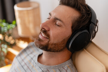 Relaxed bearded Latin man enjoying music with headphones closed eyes in cozy living room