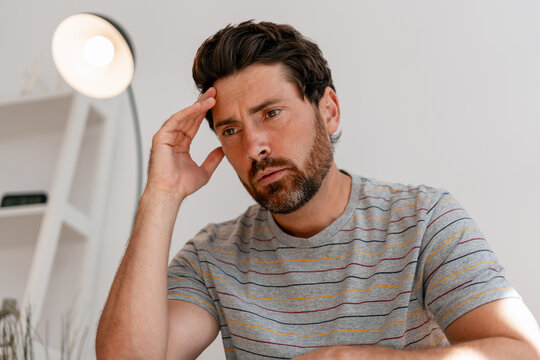 Thoughtful middle aged Latin man sitting in modern living room feeling stressed and pensive