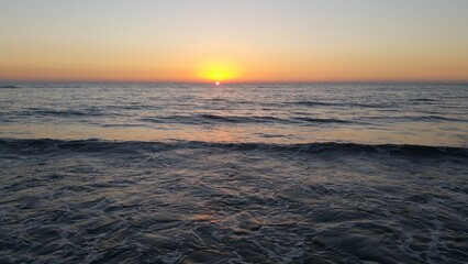 Obraz premium Sunset over the ocean horizon casting golden light across the water on a calm evening at the beach