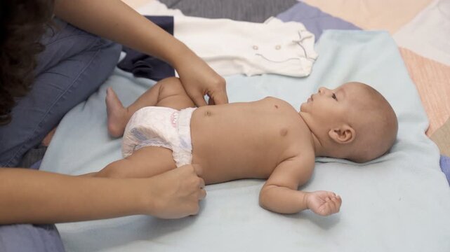 A young Indian mother puts on soft and dry diaper for her baby - young nurse with 1-month-old baby  Indian baby boy. A doula playing / cuddling a sweet child - leisure time  emotional connection  b...