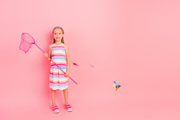 Pretty little girl smiling with a butterfly net on a pink background showcasing her cheerful and...