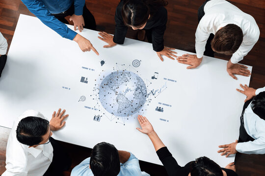 A diverse team gathers around a conference table, engaging in strategic discussions and analyzing digital graphs and projections to enhance business initiatives. Trope - Powered by Adobe