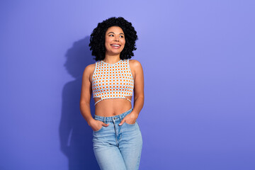 Smiling young woman in stylish attire poses casually against a vibrant purple background, exuding...