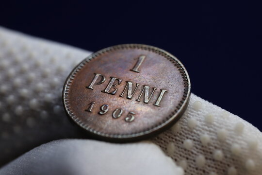 A close-up of a vintage coin showing the denomination '1 PENNI' and the year '1905', held between gloved fingers