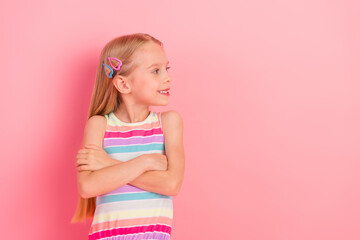 Portrait of a cheerful young girl in a colorful striped dress standing against a pink background, expressing happiness
