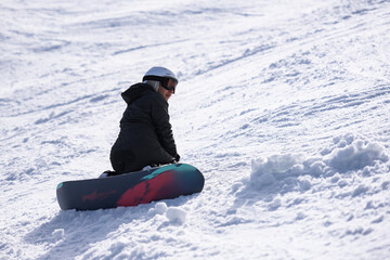 Snowboarder sitting on snowboard on sunny snowy slope