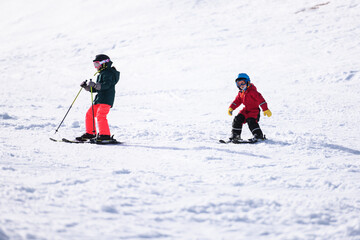 Children skiing downhill on sunny winter day