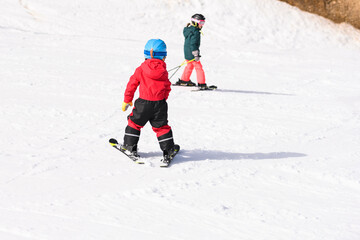 Children skiing downhill on sunny winter day