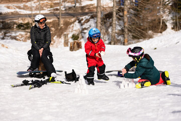 Children building snow castles while mother watches, enjoying winter vacation