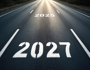 Empty asphalt road with numbers 2025 and 2027 painted on its surface, leading towards bright sunlight. This symbolizes future progression and journey.