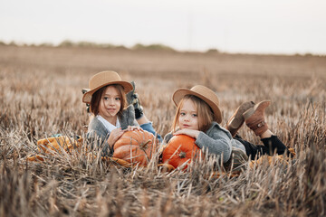 Two girls enjoying a fall day in a pumpkin field while lying on hay bales in the late afternoon light © Marko