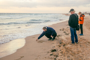 Three people walking on a sandy beach at sunset, a man drawing in the sand