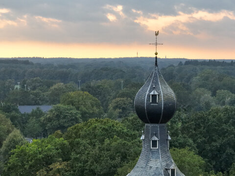 Aerial view of a church steeple rising above a sea of green trees under a dusky sky at 29 Brink, Dwingeloo, Drenthe, Netherlands.