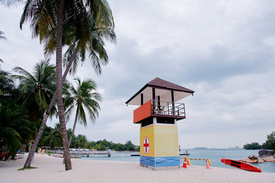 A tropical beach scene with a lifeguard tower, palm trees, and cloudy skies.