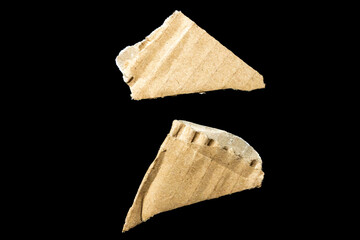 Two broken pieces of cardboard showing jagged edges and a textured surface, isolated on a black background. Ideal for discussions on recycling and waste management.