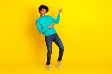 Fototapeta premium Cheerful young man in teal sweatshirt posing against a vivid yellow background conveying positivity and enjoyment