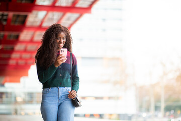 African American woman smiling while checking phone under red structure