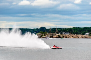 Obraz premium Red and white racing boat spraying a wake on a cloudy day