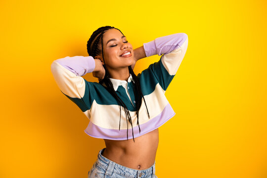 Charming young woman with braided hair enjoying leisure time against a vibrant yellow background, radiating happiness - Powered by Adobe
