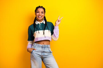 Young woman with braided hair in casual outfit is posing against a yellow background while showing...