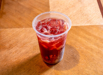 Iced Raspberry Lemonade Drink with White Foam Layer and ice cube in a Plastic Cup on wooden table side view of cold beverage