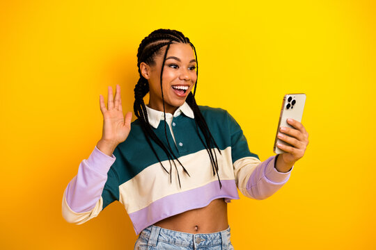 Fototapeta Cheerful young woman waving while video calling on her smartphone against a bright yellow background
