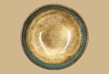 Top view of a rustic handcrafted ceramic bowl with earthy brown and green glazed finish, isolated on earth-toned background.