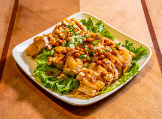 Spicy Sichuan Saliva Chicken or Kou Shui Ji with Peanuts, Chili Oil, and Scallions on Lettuce in plate on wooden board side view of main course