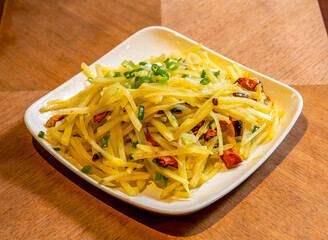 Stir fried Hot and Sour Shredded Potatoes with Chili and Scallions Suan La Tu Dou Si in plate on wooden board side view of Asian food