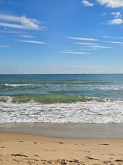 Footprints in sand on a sunny beach with foamy waves and blue sky