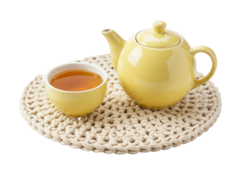 Yellow teapot and cup with tea isolated on a crocheted mat, beverage still life