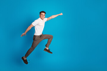 Fototapeta premium Young man leaping against a vibrant blue background in a casual outfit expressing joyful energy and dynamic creativity