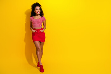 Stylish young woman posing against vibrant yellow background wearing striped top and red skirt showcasing charming personality