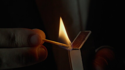 Unknown person striking match on side of box dark isolated closeup. Fire appear