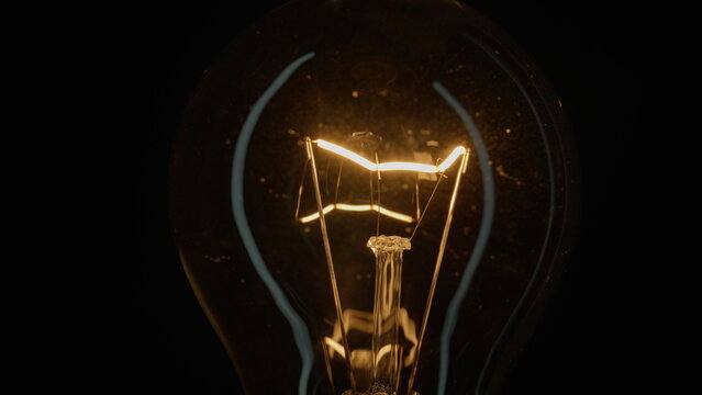 Incandescent bulb turns on and off flickers on black closeup. Flashing filament