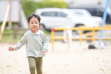 A young boy is running in a park. The park is empty and has a yellow fence. There is a car parked in the background