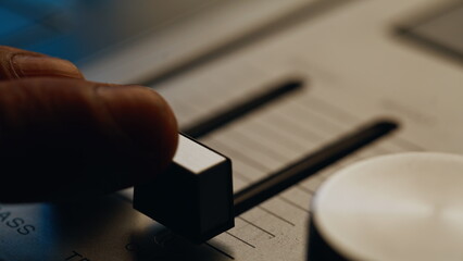 Musician hand adjusting sound balance on vintage console in dark room closeup.