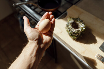 A chicken egg in a hand. A bird's nest in the table at the background. Kitchen interior. 