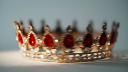 Closeup jeweled crown resting on flat surface. Red stones reflect daylight.