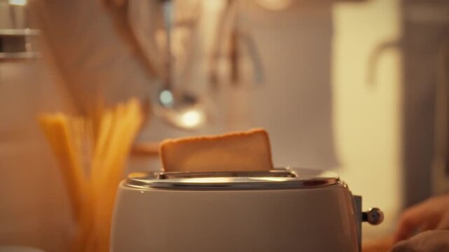 A man places a slice of bread in a toaster in a warm kitchen. The man is preparing food for dinner. The concept of cooking in the home kitchen in the evening for dinner after a day of work