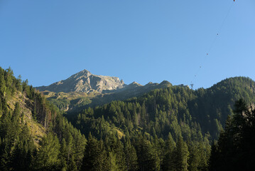 Scenic view of Ankogel (3,252 m) in the Austrian Alps, photographed from the valley cable-car station. The rugged peak rises above dense alpine forests under a clear blue sky.