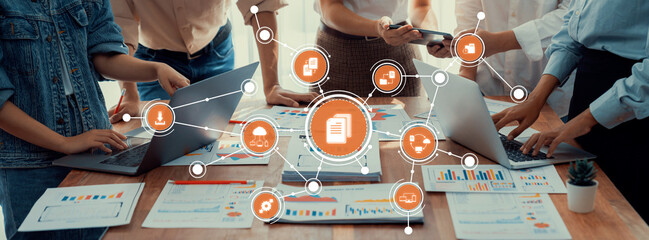 A dynamic office scene featuring individuals collaborating over laptops and documents, highlighting technology role in enhancing teamwork and strategic planning efforts. Amity