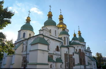 Stunning view of Saint Sophia Cathedral in Kyiv, Ukraine, showcasing its distinct green and gold domes against a bright blue sky with a hint of sunflare
