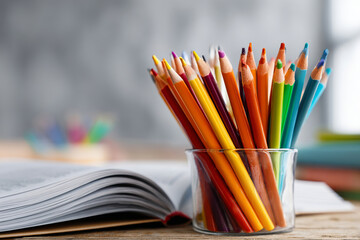 Colorful pencils in tin holder with notebook on wooden table