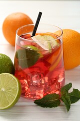 Tasty punch with ice, mint and slices of fruits in glass on white wooden table, closeup. Refreshing drink